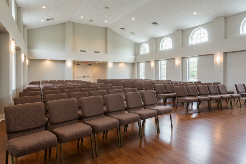 Large room with rows of brown chairs arranged for an audience, with large windows allowing natural light.